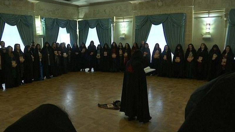 Reunidas em círculo, mulheres de capuzes e túnicas pretos, com um símbolo místico vermelho nas costas, fazem um ritual para ajudar o presidente da Rússia, Vladimir Putin.