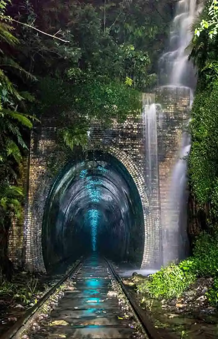 Uma passagem abandonada quase perdida em uma cascata de vegetação frondosa. Uma vez lá dentro, um brilho azul encantador ilumina o túnel escuro e úmido.